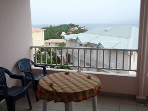 A balcony with a table and chairs, overlooking a residential area and the sea. - STUDIO ANSE MITAN TROIS ILETS MARTINIQUE (Trois Ilets)