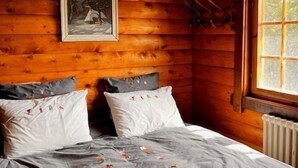 A cozy wooden cabin room with a bed, a framed picture on the wall, and a window.