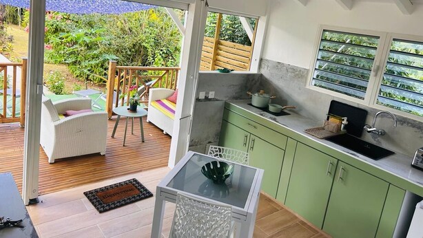 Una cocina moderna con armarios verdes, una mesa de vidrio y vistas a un jardín a través de la puerta abierta.