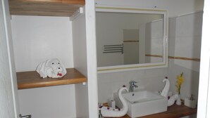 Un baño con un estante de madera que sostiene una toalla, un espejo sobre un lavamanos con un jabonera con forma de cisne, y una toalla roja en el suelo.