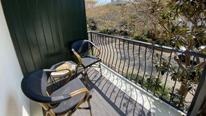 Un balcon avec deux fauteuils en osier et une petite table, donnant sur un parking et des arbres.