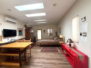 A room with a bed, a desk, a TV, and a red bench.