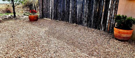 A gravel patio with a wooden fence, a potted plant, and a building in the background.