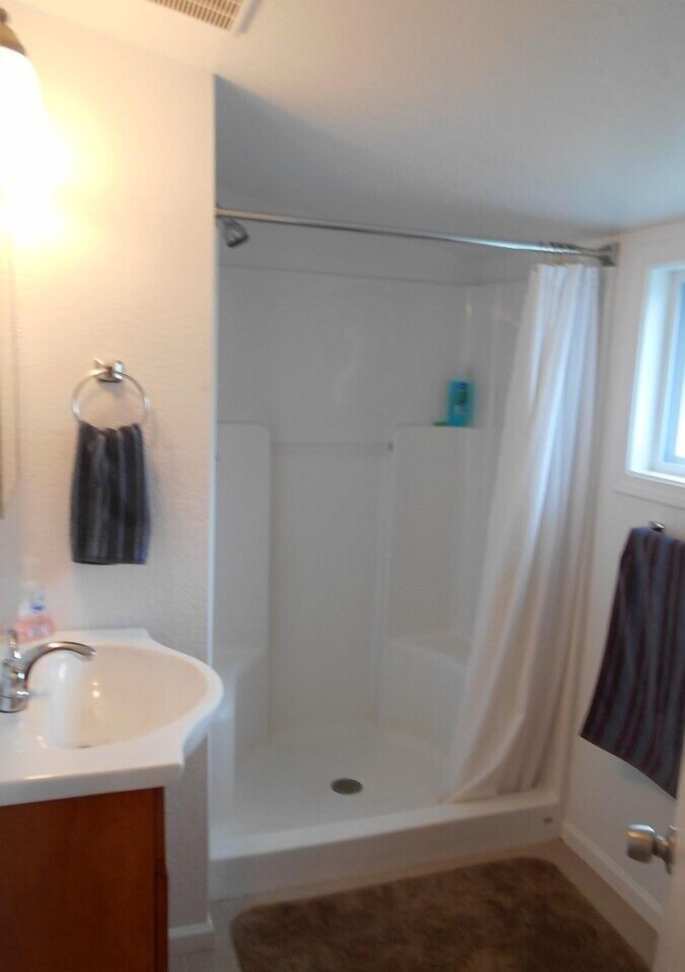 Un baño con ducha, lavamanos y un perchero para toallas.