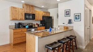 A modern kitchen with wooden cabinets, a granite countertop, a black refrigerator, and a built-in island with bar stools. - Fenced Yard | Updated Kitchen | Quiet Neighborhood (Meridian)