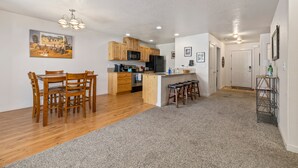 A modern kitchen with wooden cabinets, a central island with bar stools, and a dining area with a wooden table and chairs. - Fenced Yard | Updated Kitchen | Quiet Neighborhood (Meridian)