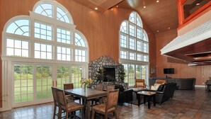 A spacious living room with a stone fireplace, large windows, and a dining area with wooden furniture. - Walk to Drakes Island Beach, Large Kitchen & Yard, Theater & Gym! Very Private (Wells)