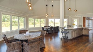A spacious kitchen with a large island, dining area with wicker chairs, and large windows offering views of the outdoors. - Walk to Drakes Island Beach, Large Kitchen & Yard, Theater & Gym! Very Private (Wells)
