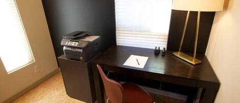 Un pequeño espacio de oficina con un escritorio, una silla, una impresora, una lámpara y una ventana.