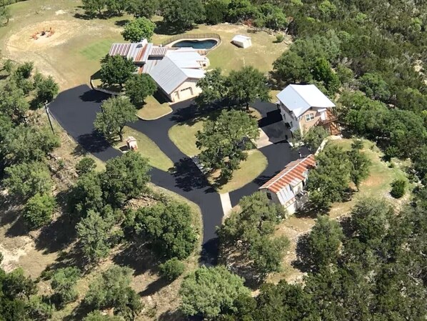 An aerial view of a residential area with multiple houses, a winding driveway, and a small pond.
