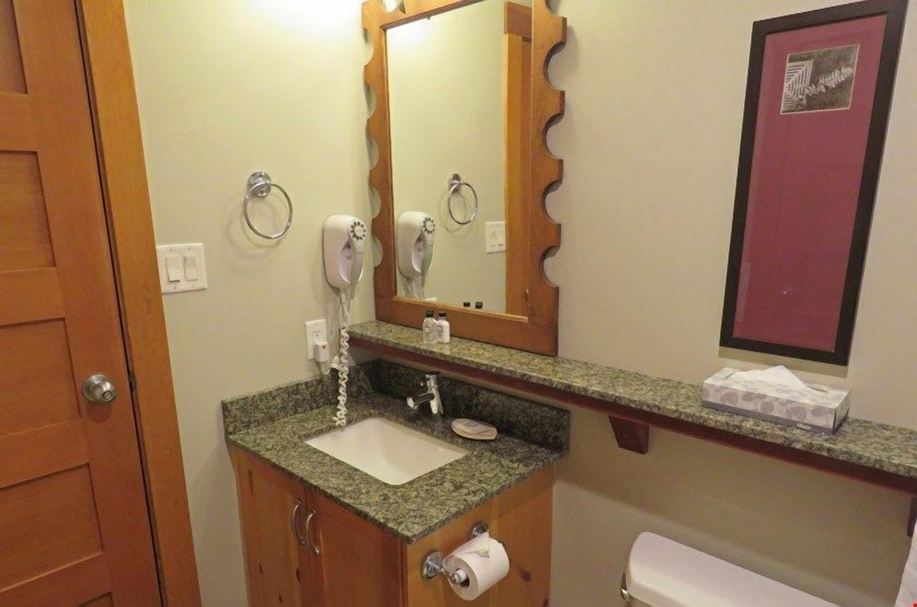 A bathroom with a sink, mirror, towel ring, and toilet paper.