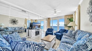 Amplia sala de estar con televisor grande, chimenea y balcón con vista al mar.