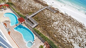 Un resort con dos piscinas, playa y un paseo marítimo que lleva a la playa.