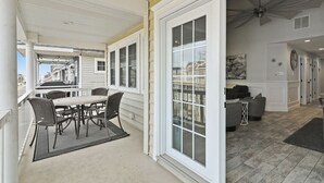 Uma sala de estar ampla com uma grande porta de vidro deslizante que dá para uma varanda, uma área de jantar com mesa e cadeiras, e uma ventoinha de teto moderna.