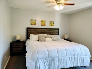 A neatly made bed with a white duvet, two bedside tables with lamps, and a ceiling fan. - Spacious 2 Bedroom Condo near Golf Country Club (Brownsville)