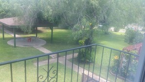Un balcón con vistas a un jardín cuidado, un espacio de estar cubierto y un sendero.