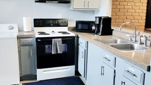 Cocina compacta con alacenas blancas, estufa, microondas y pileta.