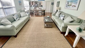 A spacious living room with a large woven rug, two sofas, a coffee table, and a dining area with a chandelier. - Sandy Feet Retreat-1/2 Block to Beach, Pet Friendly, Wi-Fi & Optional GC Rental  (Surfside Beach)