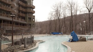 A swimming pool with a curved design, surrounded by a stone walkway and a wooden fence. - Luxury Studio Ski in -ski out Mt Mansfield Views, Mountain Golf Course Access (Stowe)