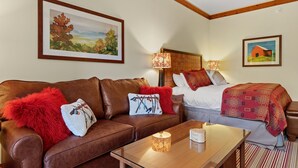 A cozy room with a brown leather sofa, a wooden coffee table, and a bed with a red blanket. There are two wall-mounted lamps and a framed painting above the sofa. - Luxury Studio Ski in -ski out Mt Mansfield Views, Mountain Golf Course Access (Stowe)