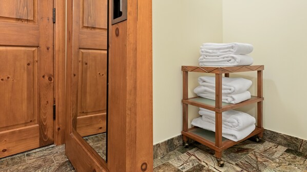 Una puerta de madera con un pequeño ventanal, un perchero de madera con toallas dobladas y un piso de baldosas.