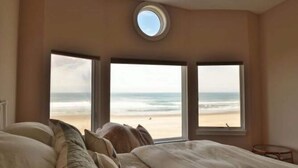 A bedroom with a large bed, a round skylight, and three windows offering a view of the beach.
