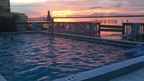 En pool med liggestole og udsigt til solnedgang over vandet.