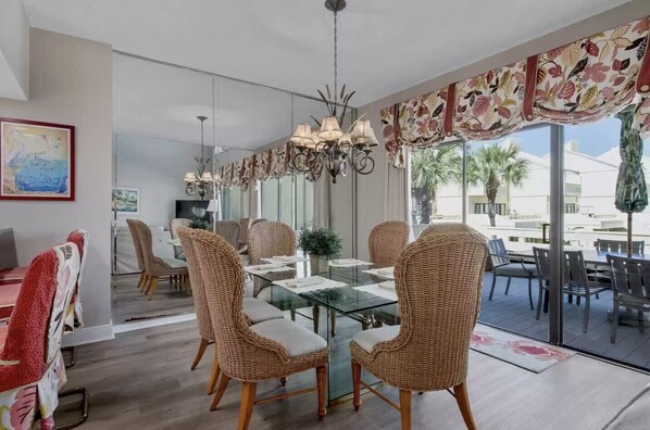A modern dining area with wicker chairs, a glass table, and a view of palm trees outside.