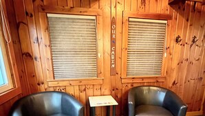 Une cabane avec deux fauteuils en cuir, une petite table et des murs en bois équipés de stores.