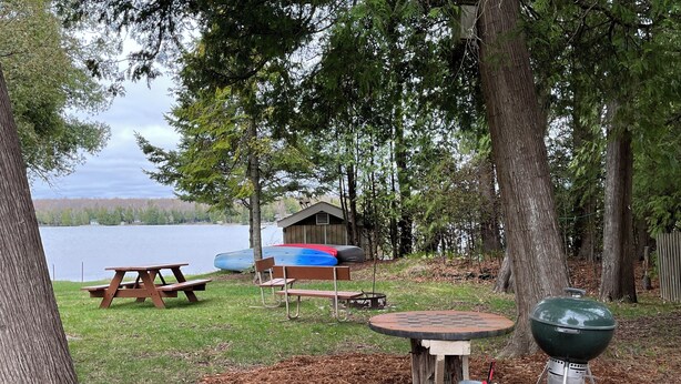 Un terrain de camping au bord du lac, équipé de tables de pique-nique, d’un barbecue et d’un abri.