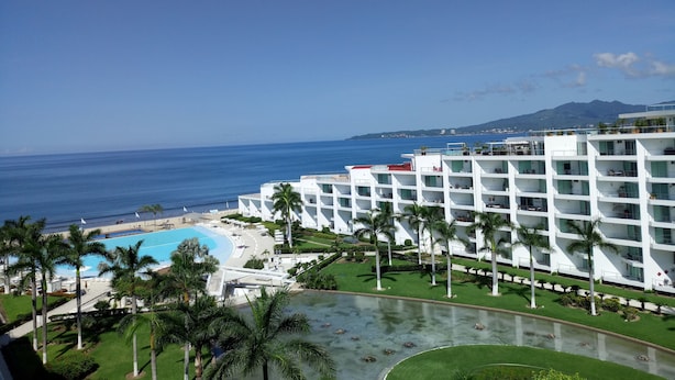 A resort with a pool, palm trees, and a view of the ocean.