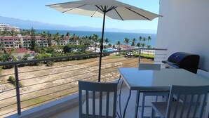 A balcony with a table, chairs, and a grill.