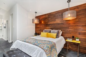 Relax in a serene bedroom with a large bed, pendant lights, and a stylish wooden panel above.