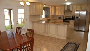 A kitchen with a central island, wooden dining table, chairs, and a refrigerator. - Wonderful Whispering Hills (Tucson)