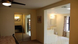 A hotel room with a bed, a ceiling fan, a large mirror, a bathroom with a bathtub, and a window with curtains. - Wonderful Whispering Hills (Tucson)