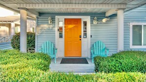 Een huis met een fel oranje voordeur, twee lichtblauwe Adirondack-stoelen en een overdekte veranda met zuilen.