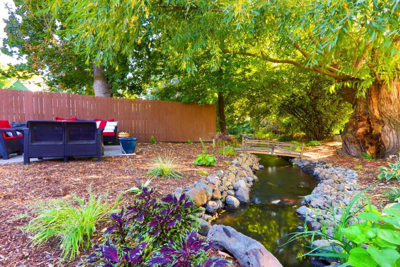 A backyard with a small pond, a wooden bridge, and outdoor furniture.