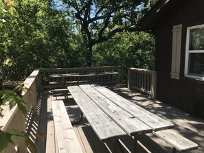 Eine Holzterrasse mit Picknicktischen und Bänken, umgeben von Bäumen.