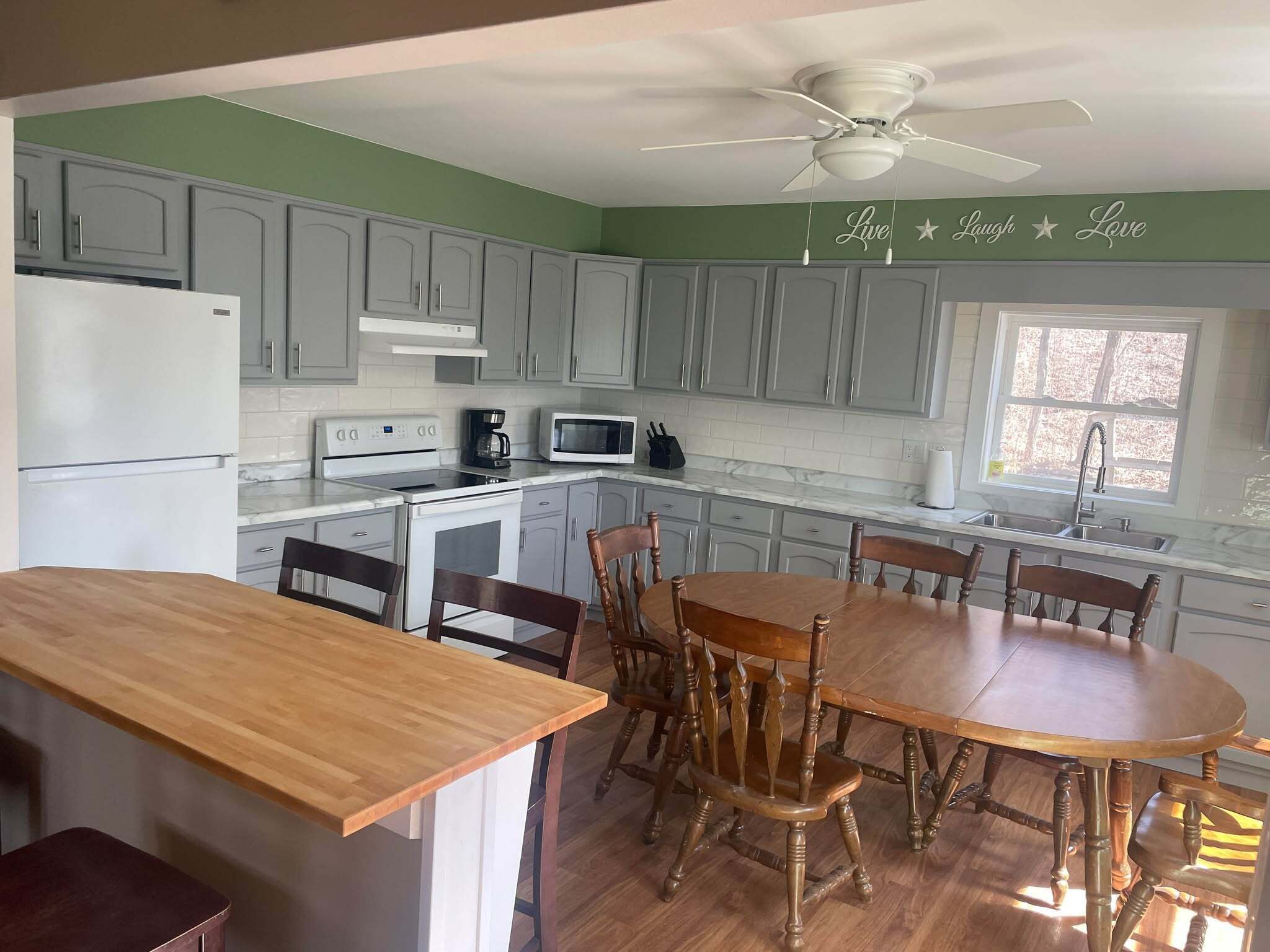 Une cuisine avec des meubles de couleur grise, un réfrigérateur blanc, une cuisinière, un four à micro-ondes et une table à manger avec des chaises en bois.