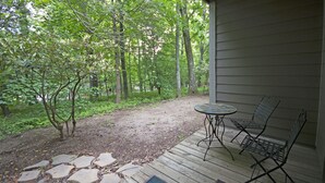 Une terrasse en bois avec une table et deux chaises, entourée d’une zone boisée.