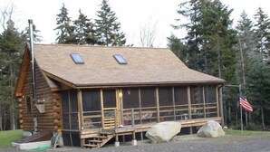 A log cabin with a steep roof, large windows, and an American flag. - Hand Crafted Log Cabin (St George)