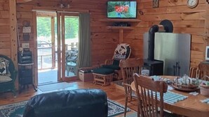 A cozy cabin interior with a dining area, wooden walls, a television, and a fireplace. - Hand Crafted Log Cabin (St George)