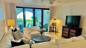Ein Wohnzimmer mit einer Couch, einem Couchtisch mit Blumen, einem Fernseher und einem Sessel.