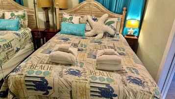 A hotel room with two beds, each with a beach-themed bedspread and matching pillows. There are two bedside lamps and a starfish decoration on the headboard.