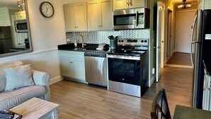 A modern kitchen with stainless steel appliances, a dishwasher, and a microwave. There is a clock on the wall and a sign that says "BEACH". - SeaGem-Oceanview! Steps to ocean Many Upgrades New Reno (Hilton Head Island)