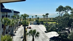 A view of a building with a covered outdoor area, palm trees, and a distant view of a body of water. - Salty Shores! -Incredible ocean views (Hilton Head Island)