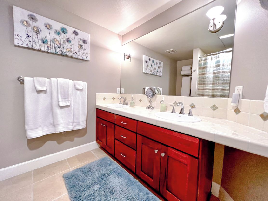 A bathroom with a double sink, red cabinets, a blue rug, and two wall-mounted towels.