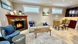 A living room with a fireplace, a sofa, a coffee table, and a dining area with chairs and a table. - 180° Space Needle, Lake Union & Downtown Views! (Seattle)
