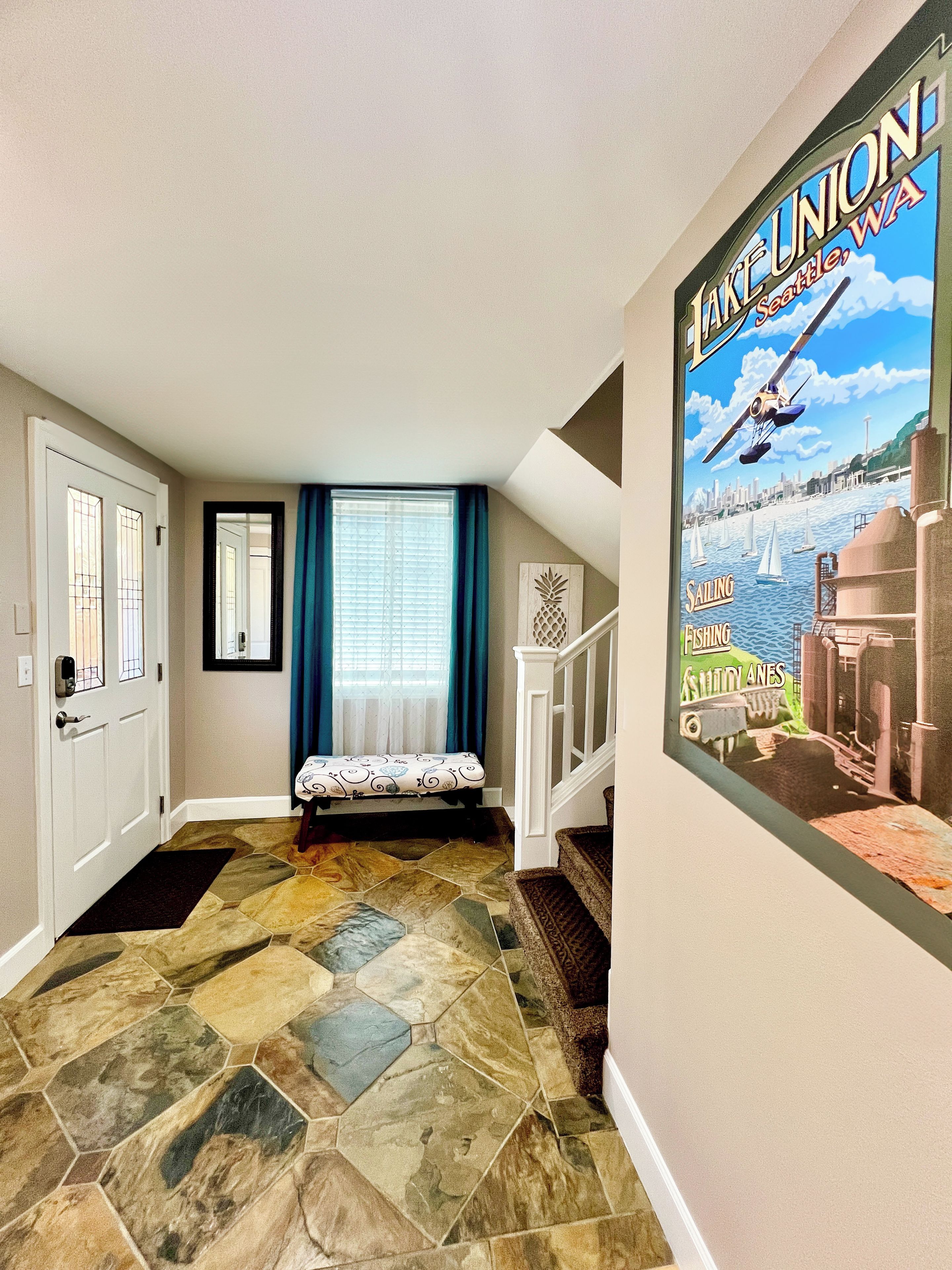 A hallway with a stone-patterned floor, a bench, a staircase, and a poster of a sailing scene.