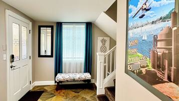 A hallway with a stone-patterned floor, a bench, a staircase, and a poster of a sailing scene.